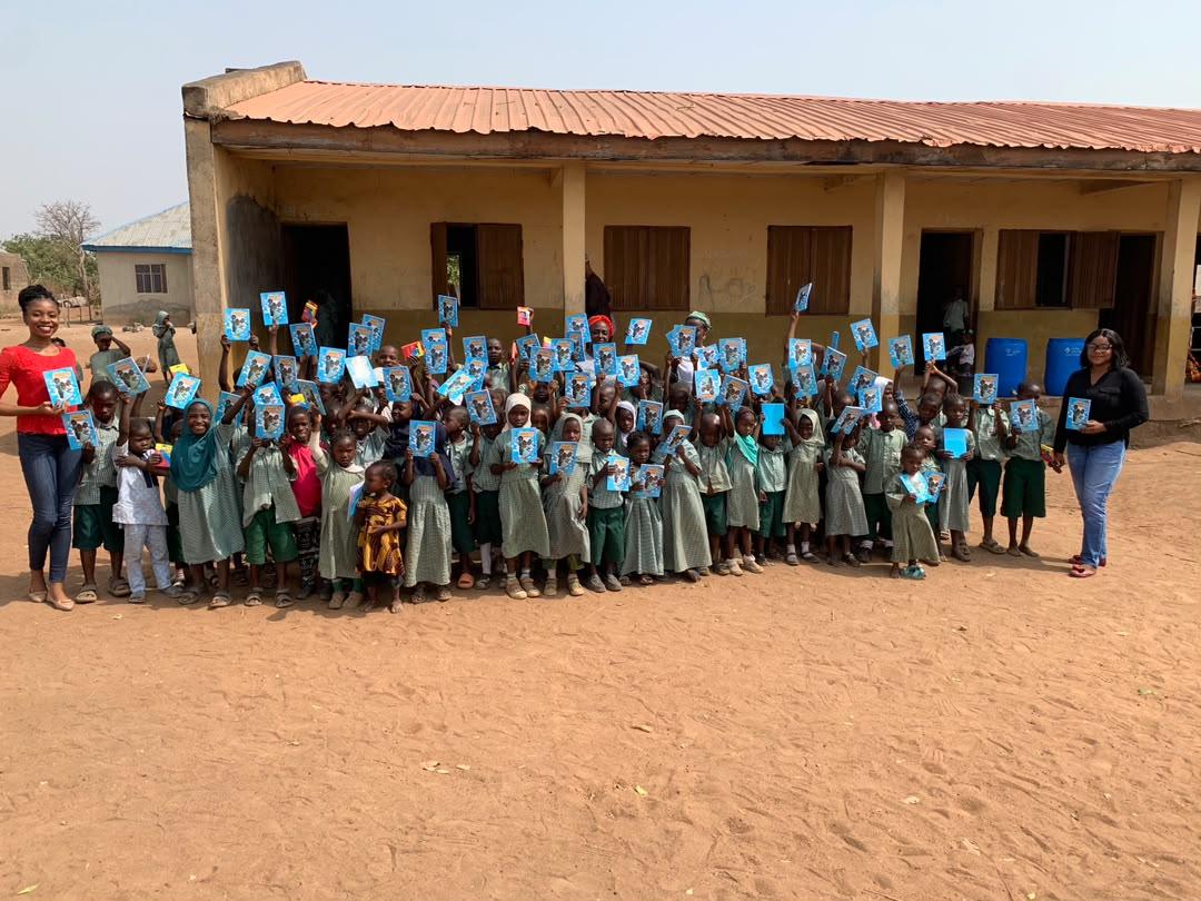 Children in green uniforms holding up their books