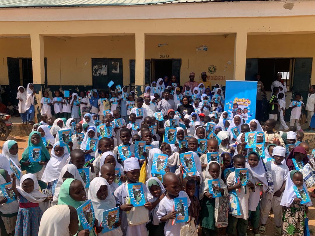 A schoolyard full of children holding up Amira books